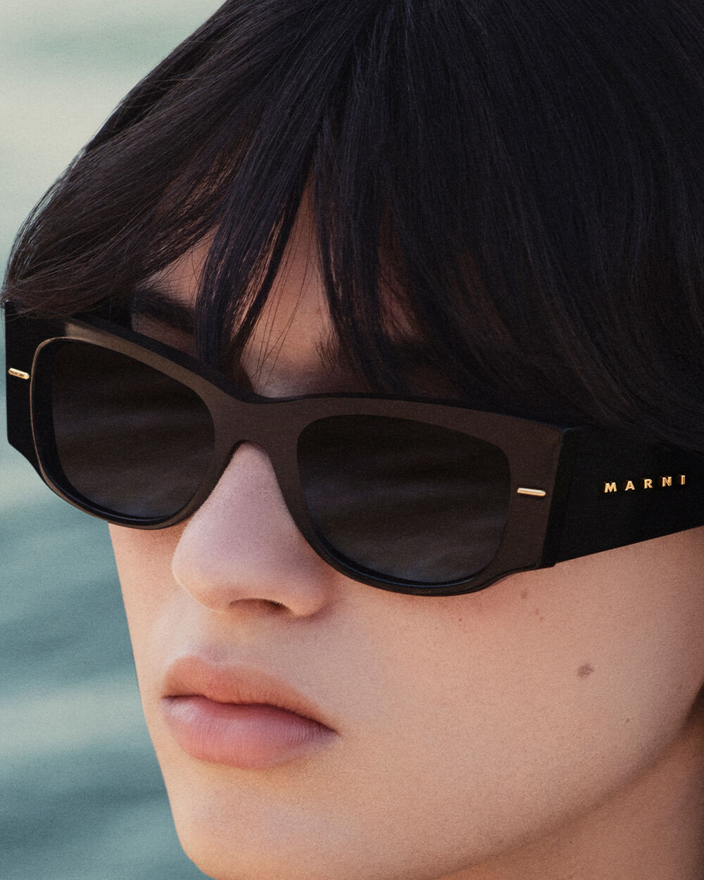 Close-up of a model wearing black Marni sunglasses with gold logo detail