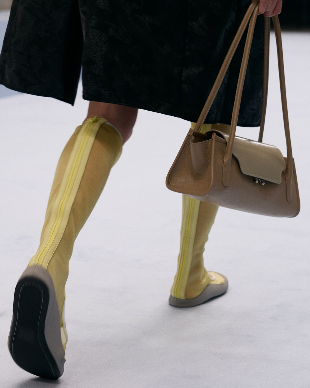 Model carrying a beige Marni Trunkette bag, paired with yellow mesh knee-high boots