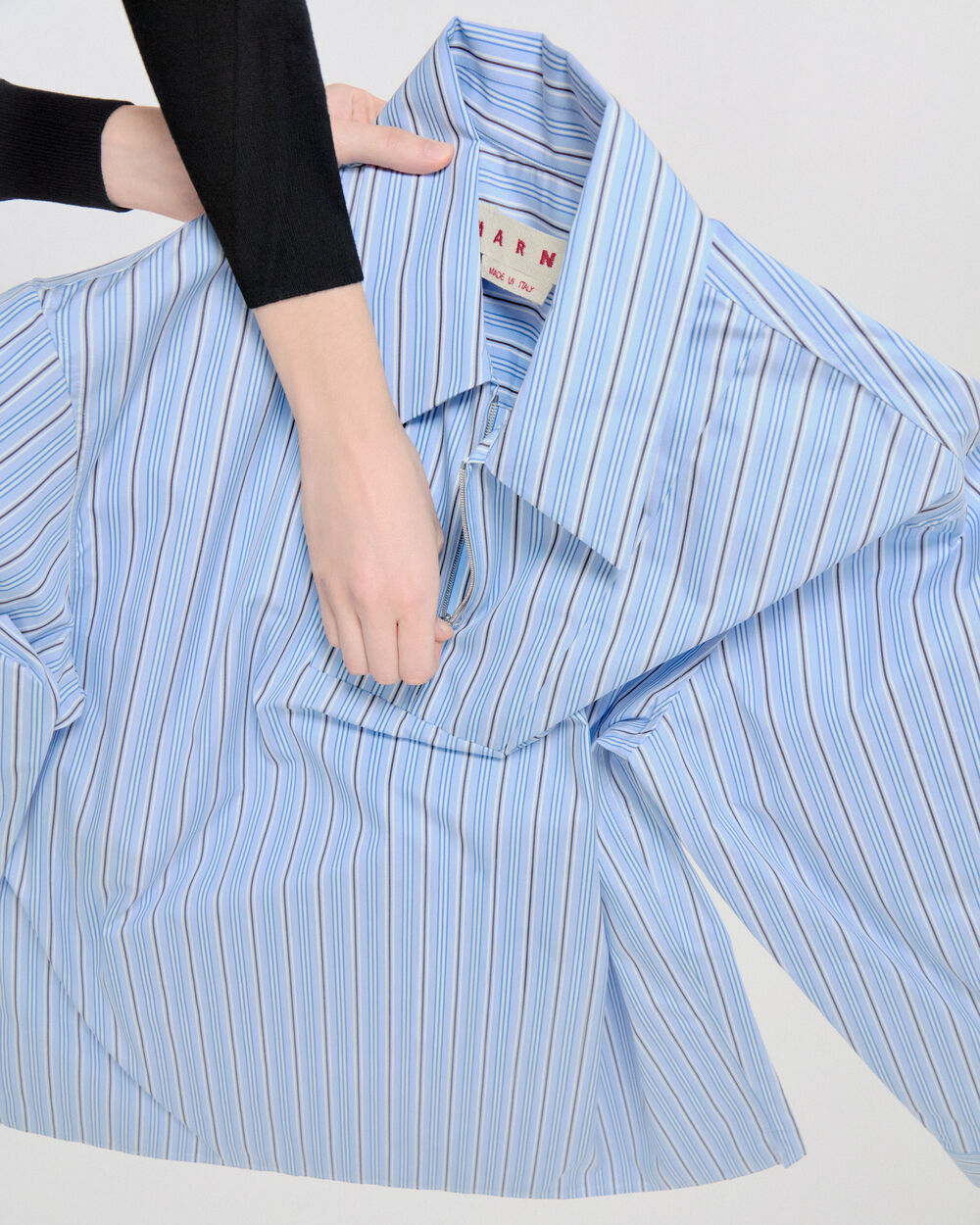 Blue striped Marni shirt held by a model, highlighting the oversized silhouette and pointed collar