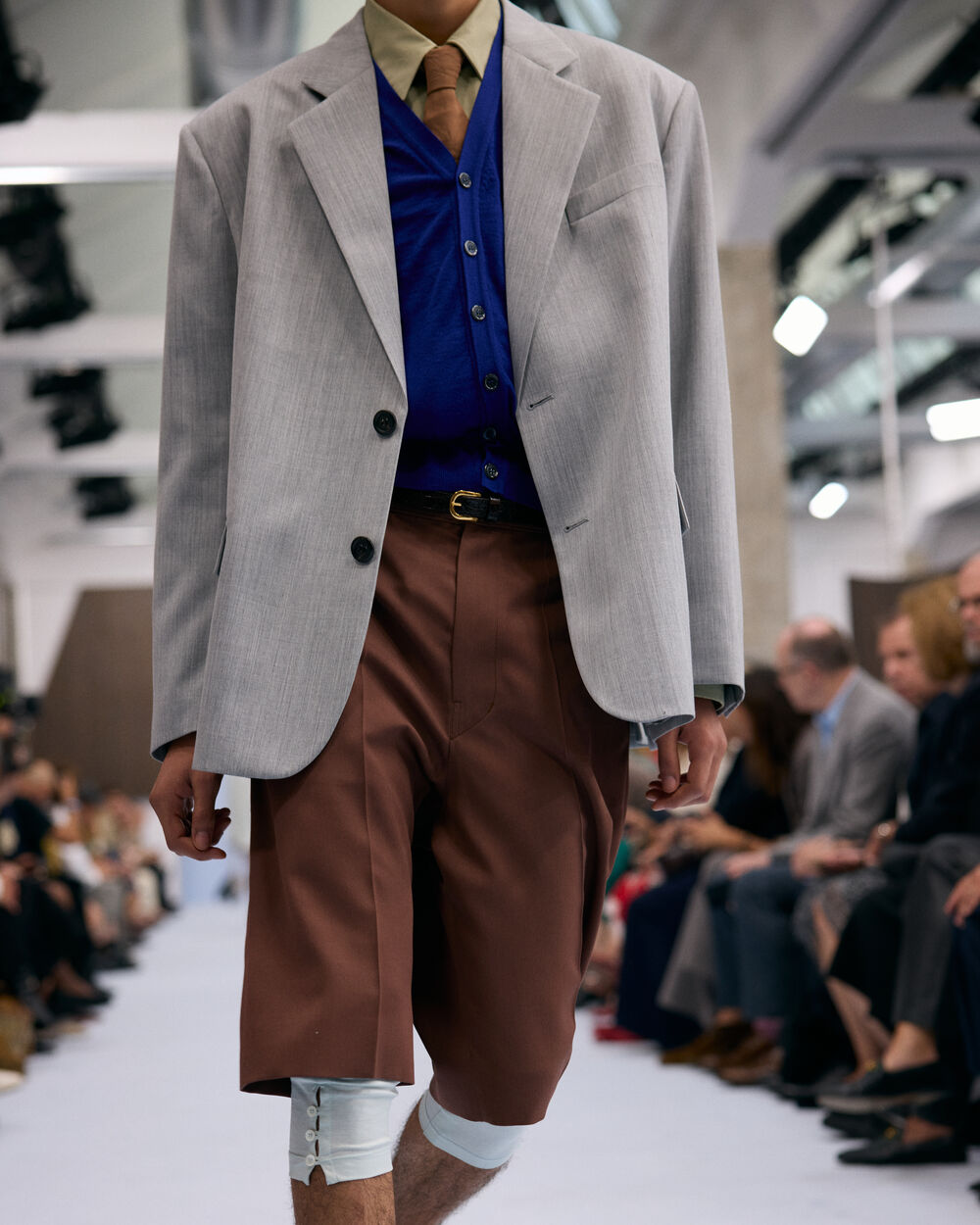 Model wearing a grey blazer with blue vest and brown tailored shorts