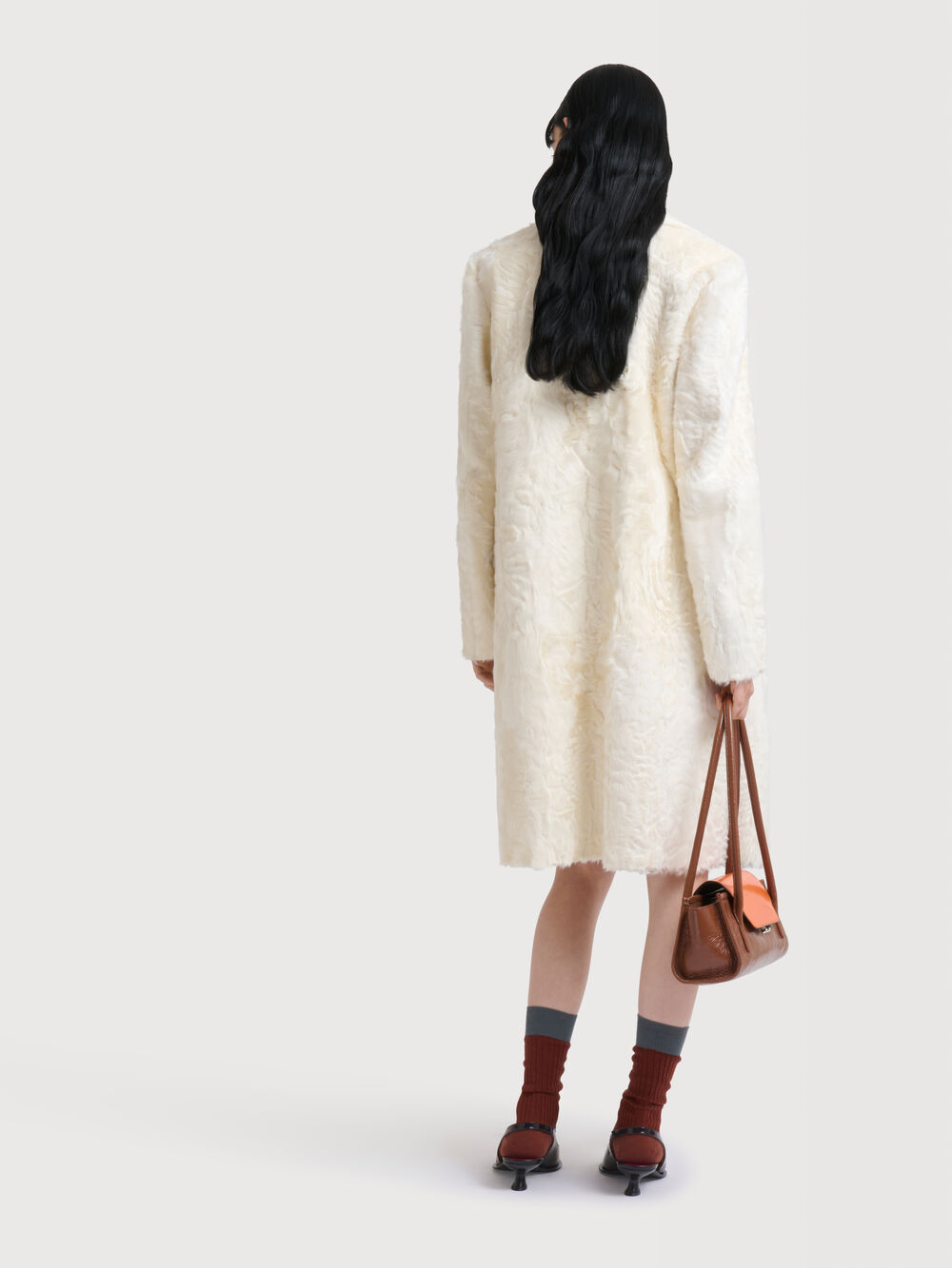 Model wearing a white textured coat and carrying a brown Marni Trunkette bag